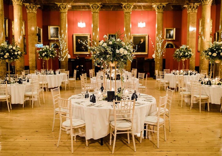 Room set up for a wedding with round tables and chairs and large floral displays 